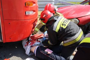 dwóch strażaków wyciąga spod autobusu osobę poszkodowaną w wypadku