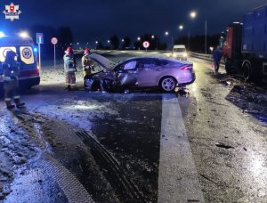 miejsce zdarzenia drogowego, uszkodzone dwa pojazdy, strażacy stojący obok samochodu i karetka