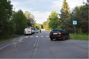 miejsce wypadku drogowego, skrzyżowanie i dwa uszkodzone pojazdy, w oddali funkcjonariusz policji i radiowóz