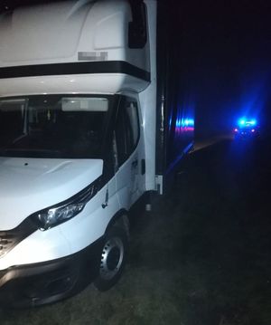 samochód Iveco z urwanym lewym lusterkiem, w oddali radiowóz z włączonymi sygnałami świetlnymi