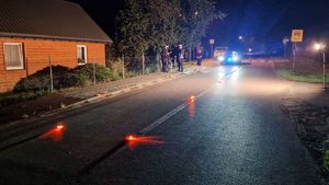 dwóch policjantów wykonujących oględziny jednośladu biorącego udział w zdarzeniu drogowym, w oddali radiowóz w włączonymi sygnałami świetlnymi, na jezdni elementy świetlne zabezpieczające miejsce wypadku