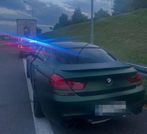 zatrzymany do kontroli drogowej pojazd BMW w oddali policyjny radiowóz z włączonymi światłami świetlnymi