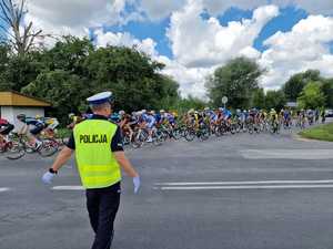 policjant kieruje ruchem, w tle peleton kolarzy