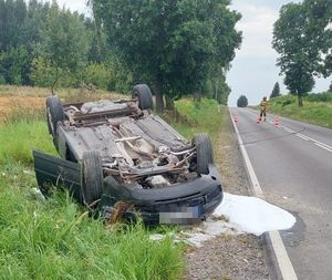 samochód na pobczu po dachowaniu, w oddali strażak kieruje ruchem