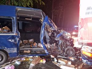 uszkodzony bus który uderzył w tył naczepy ciężarówki, w oddali wóz strażacki z włączonymi sygnałami świetlnymi