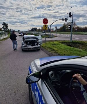 fragment radiowozu w oddali uszkodzony Volkswagen obok mężczyzna