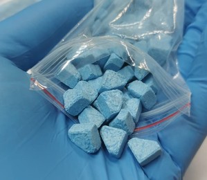 tabletki ecstasy wysypane z woreczka strunowego na rękę w niebieskiej rękawiczce