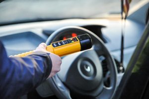ręka policjanta z urządzeniem do pomiaru trzeźwości w tle kierownica pojazdu