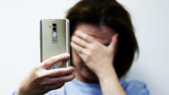 kobieta trzymająca w dłoni telefon, a drugą ręką zasłania twarz