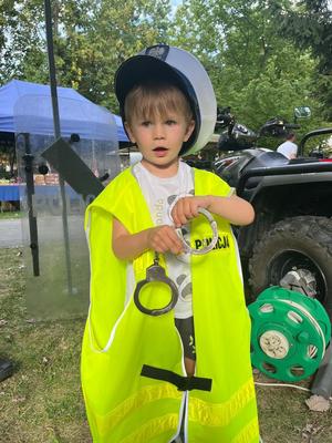 dziecko ubrane w kamizelkę i czapkę policyjną z kajdankami w rękach