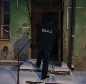 policjant przed budynkiem , sprawdza miejsca gdzie mogą przebywać osoby narażone na wychłodzenie