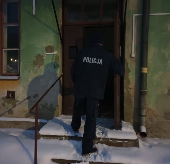 policjant przed budynkiem , sprawdza miejsca gdzie mogą przebywać osoby narażone na wychłodzenie