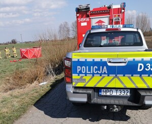 radiowóz oznakowany obok straży pożarnej, w oddali parawan straży pożarnej na polu