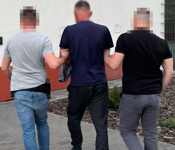 policjanci prowadzą osobę zatrzymają poszukiwaną listem gończym