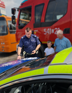 policjant przy radiowozie, obok mężczyzna i chłopiec
